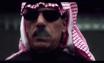a man wearing a keffiyeh and sunglasses smoking a cigarette .