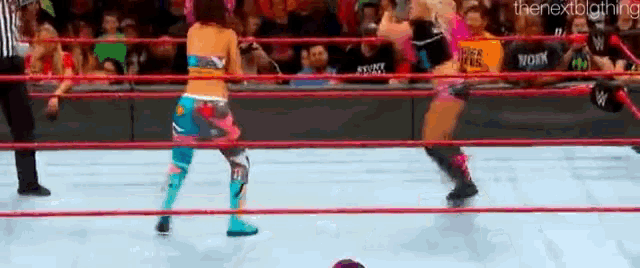 two women are wrestling in a ring with a referee and a crowd watching .