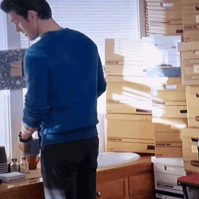 a man in a blue sweater stands in front of a pile of storage boxes