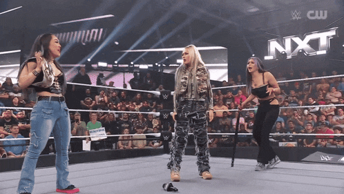 three women are standing in a wrestling ring with nxt written on the wall in the background