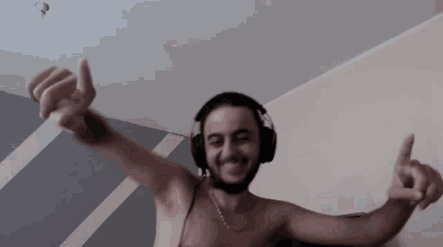 a shirtless man wearing headphones is dancing with his arms in the air