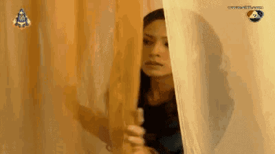 a woman peeking out from behind a curtain with a watermark that says ' www.tv3.com ' on it
