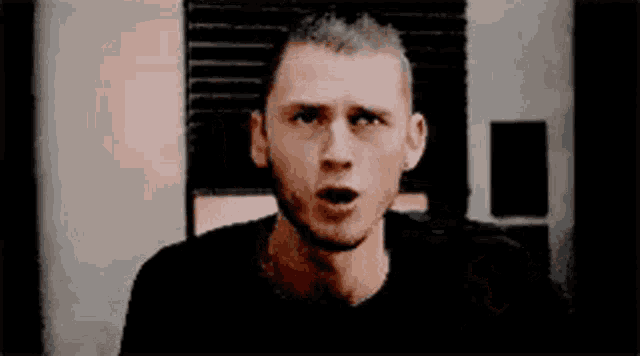 a man in a black shirt is making a funny face while standing in front of a window .