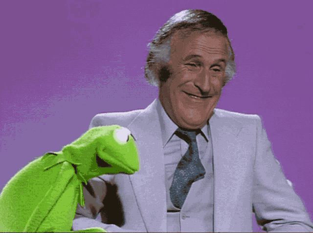 a man in a suit and tie is talking to a green kermit the frog puppet