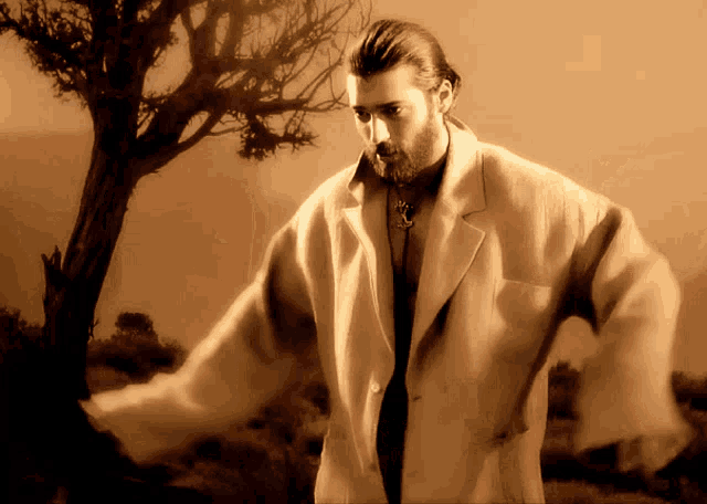 a man in a white coat stands in front of a tree in the desert