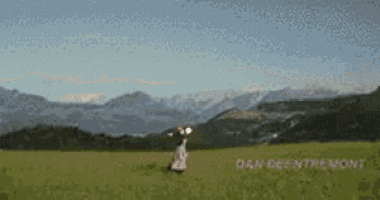 a woman is standing in a grassy field with mountains in the background