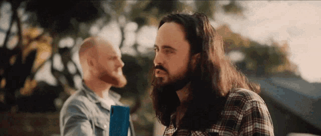 a man with long hair and a beard stands next to another man with a bald head