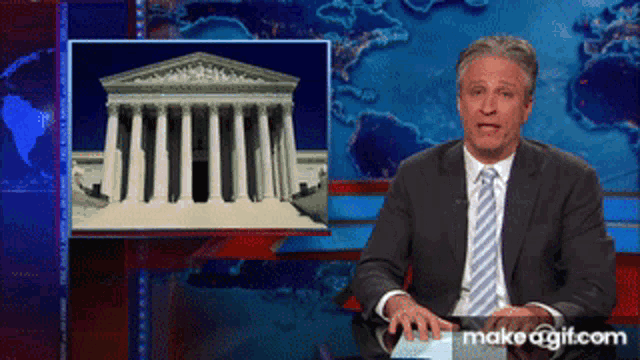 a man in a suit and tie stands in front of a picture of the supreme court