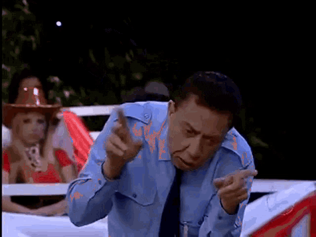 a man in a blue shirt and tie is pointing at the camera .
