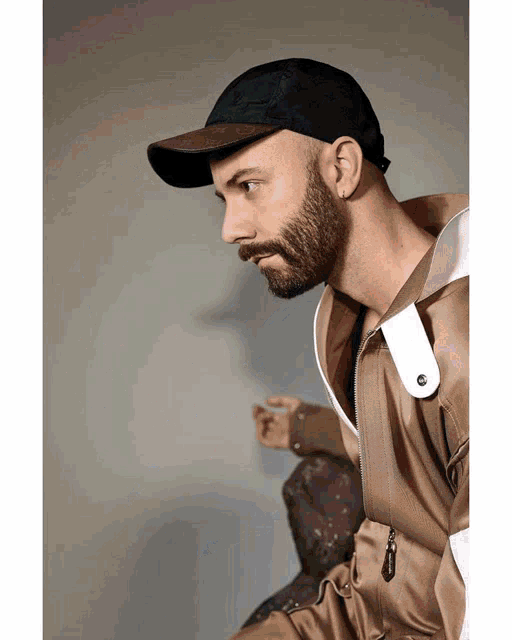 a man with a beard wearing a black hat and a brown jacket