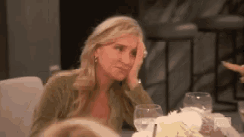 a woman is sitting at a table with her hand on her forehead and a glass of water .