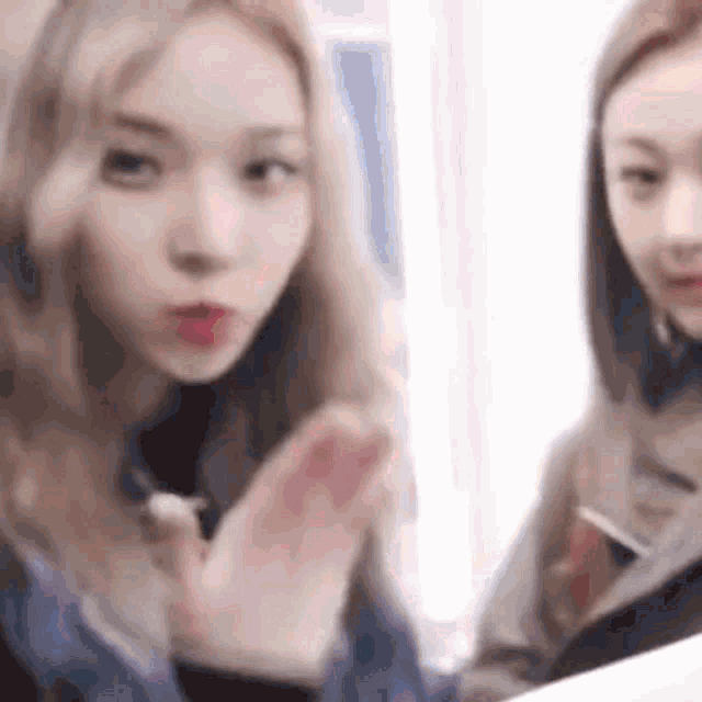two girls are sitting next to each other and one of them is blowing a kiss at the camera .