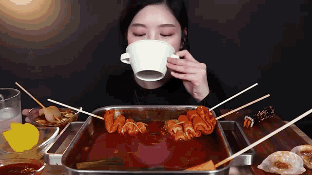 a woman drinking a cup of coffee while eating food on sticks