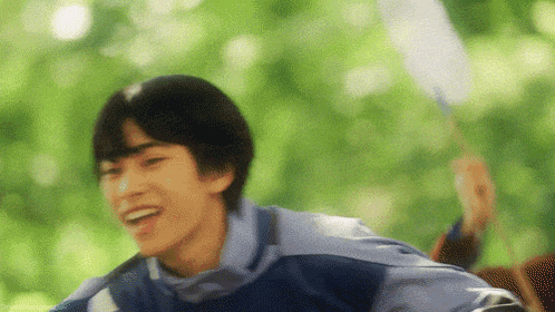 a young man is smiling while holding a badminton racket in front of trees .
