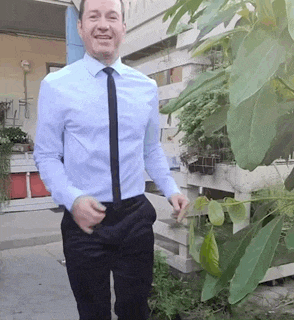 a man wearing a blue shirt and black tie is standing in front of a fence .