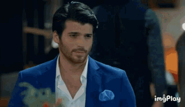 a man in a blue suit and white shirt with a blue pocket square is standing in a room .
