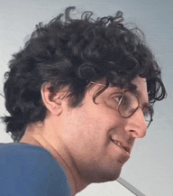 a man with curly hair and glasses is smiling and wearing a blue shirt
