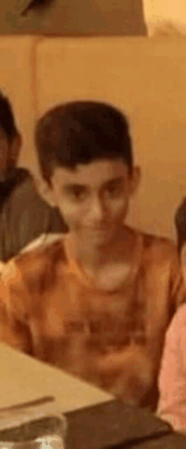 a young boy is sitting at a table in a restaurant with other people .