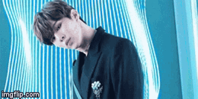 a young man in a black suit is standing in front of a blue wall .