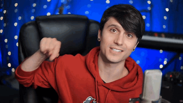 a young man wearing a red hoodie is sitting in front of a microphone