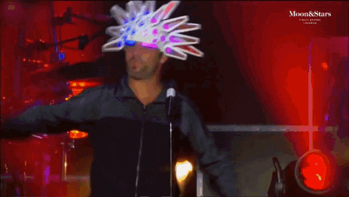 a man wearing a colorful hat stands in front of a microphone with the words moon & stars on the bottom right