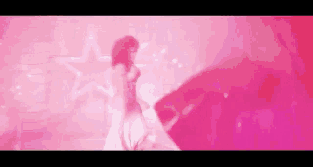 a woman in a white dress is dancing in front of a pink background with stars .