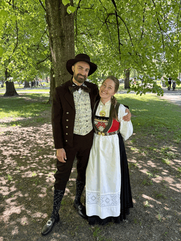 a man and a woman posing for a photo in a park