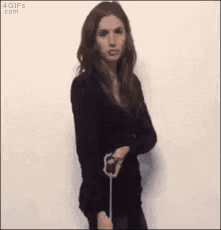 a woman in a black dress is standing in front of a white wall and holding a cell phone .