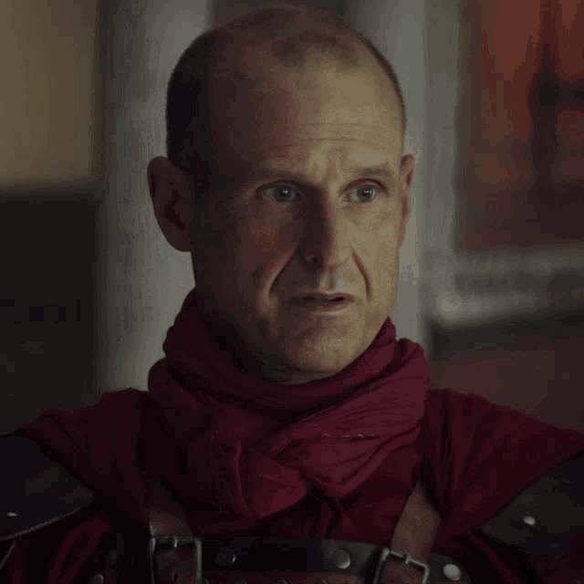 a man with a red scarf around his neck looks at the camera