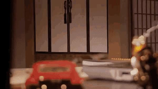 a red toy car is sitting on a table in a room with a clock on it .