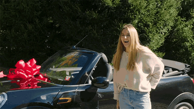 a woman is standing in front of a convertible car with a red bow on it