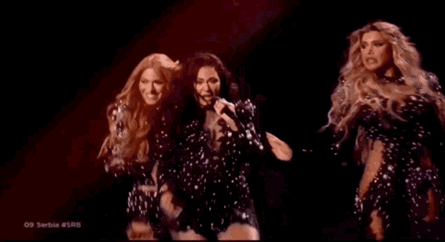 three women are standing next to each other and one of them is singing into a microphone .