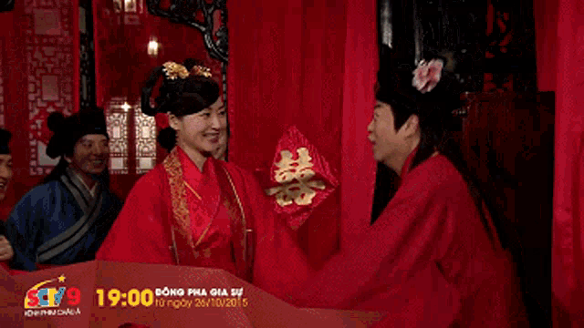 a man wearing a red robe and a black hat stands in front of a building with asian writing on it