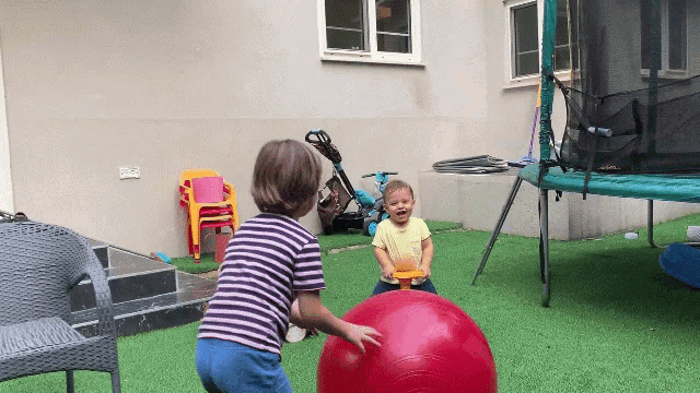 two children are playing with a large red ball