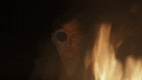 a man with a patch on his eye is looking at a fire .