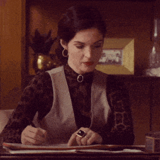 a woman in a leopard print shirt and vest is sitting at a desk writing in a notebook .