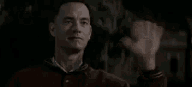 a man in a red jacket is waving his hand in a dark room .