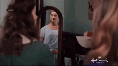 a woman is looking at herself in a bathroom mirror .