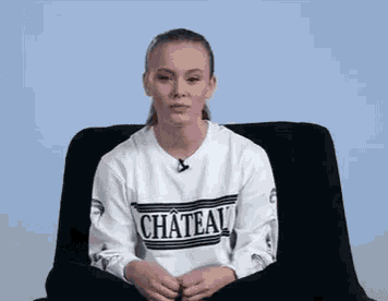 a woman is sitting in a chair wearing a white sweatshirt with the word chateal on it .
