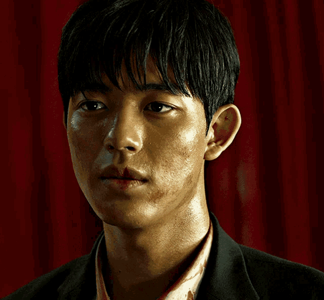a close up of a man 's face with a red curtain in the background