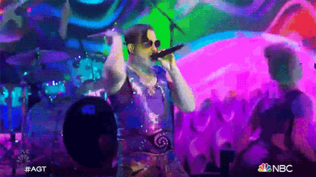 a man is singing into a microphone on a stage in front of a crowd of people .