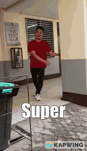 a man in a red shirt is walking down a hallway with the words super written on the ground .