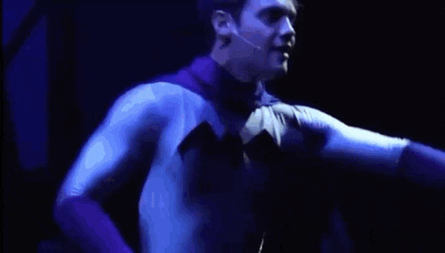a man in a batman costume is standing in front of a microphone on a stage .