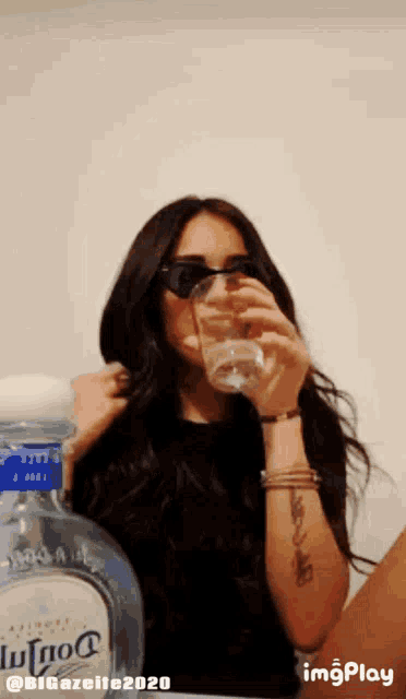 a woman is drinking a glass of water next to a bottle of tequila