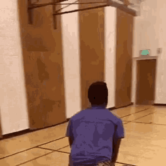 a man in a blue shirt is kneeling on a basketball court .