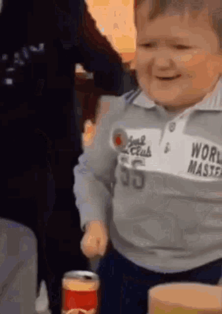 a baby is holding a can of soda and smiling while wearing a world master shirt .