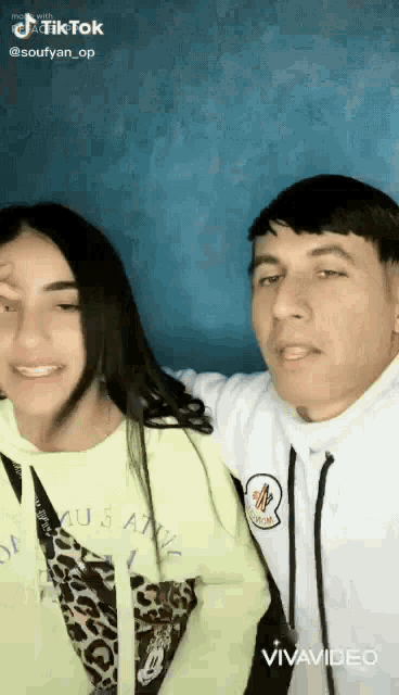 a man and a woman are posing for a picture together . the woman is wearing a neon green hoodie .