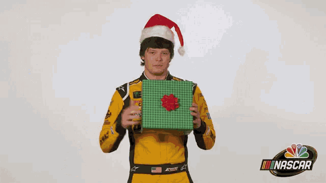 a man wearing a santa hat is holding a gift box in front of the words merry christmas nascar .