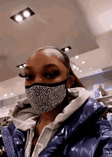 a woman wearing a rhinestone mask and a blue jacket is standing in a store .