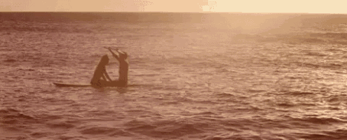 two people are riding a paddle board in the ocean .